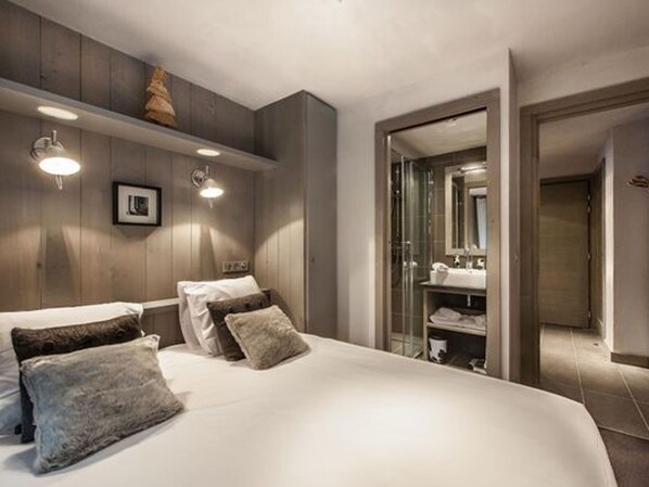 A modern bedroom with a large bed, a wooden headboard, and a glass shower enclosure.