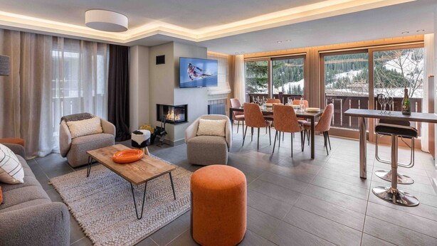 Un salon moderne doté d’une cheminée, de sièges confortables, d’un coin repas et de grandes fenêtres offrant une vue sur l’extérieur.