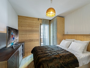 Un dormitorio con cabecera de madera, cama con sábanas blancas, televisor sobre un tocador de madera y una lámpara colgante.