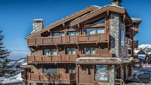 A multi-story wooden building with balconies, stone chimneys, and a view of snow-covered mountains.