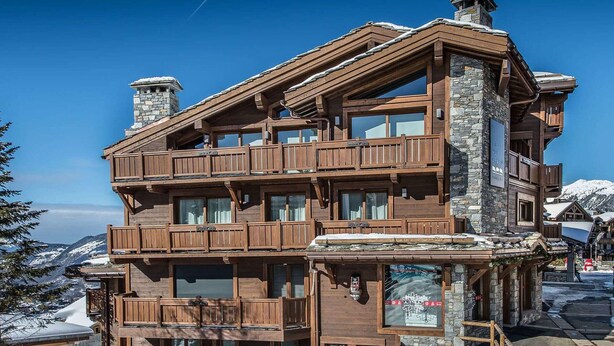 A multi-story wooden building with balconies, stone chimneys, and a view of snow-covered mountains. - Cozy apartment in Courchevel with spacious bedroom and parking (Courchevel 1650)