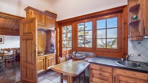 A wooden kitchen with a large window, a dining table, and cabinets. - Charming Savoyard chalet, sleeps 12, sauna, piste access, Moriond (Courchevel 1650)