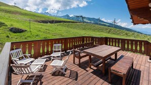 A wooden deck with outdoor furniture, overlooking a green landscape with mountains in the distance. - Charming Savoyard chalet, sleeps 12, sauna, piste access, Moriond (Courchevel 1650)