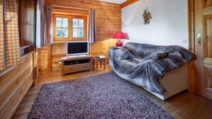 A cozy log cabin room with a television, a red lamp, a grey sofa, and a patterned rug. - Charming Savoyard chalet, sleeps 12, sauna, piste access, Moriond (Courchevel 1650)
