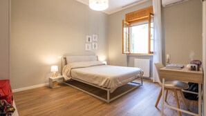 Une chambre à coucher comprenant un lit, une table de chevet, une lampe, une fenêtre avec des rideaux et un bureau avec une chaise.
