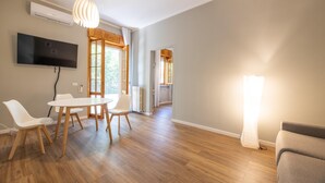 Un salon moderne doté d’un téléviseur à écran plat, de planchers en bois, d’une table à manger avec des chaises et d’un canapé.