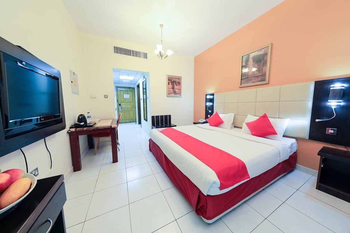 A hotel room with a large bed, a desk, a television, and a door leading to a balcony.
