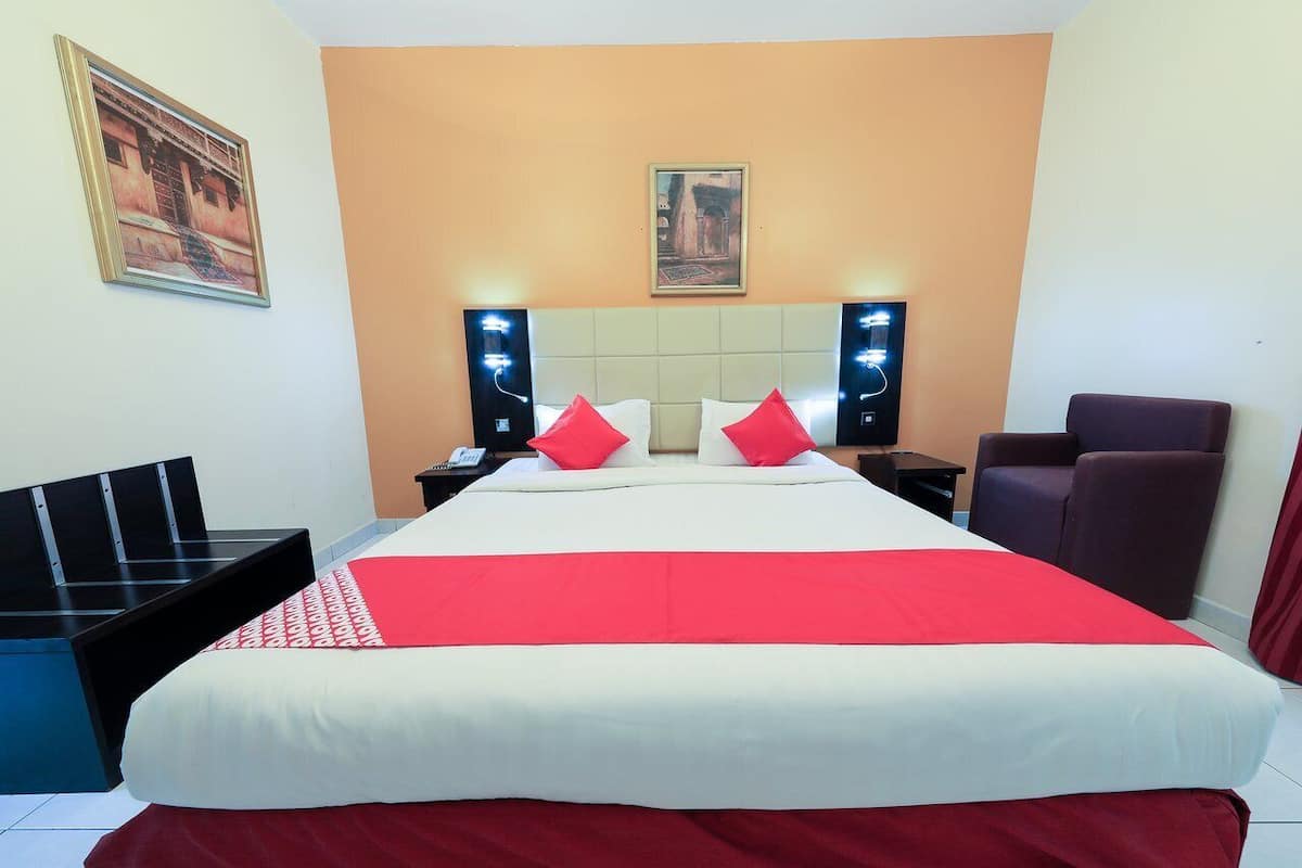 A hotel room with a large bed, two bedside tables, a chair, and a painting on the wall.