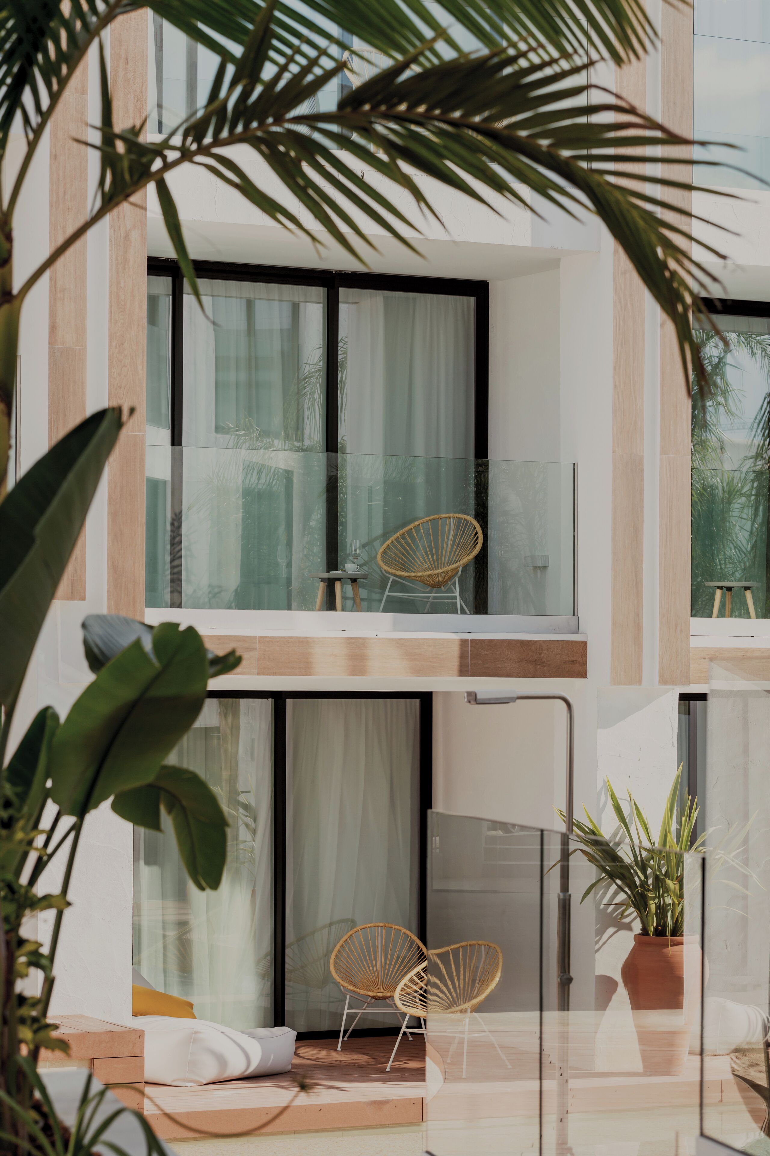 Ein moderner Balkon mit Glastrennwand, zwei Korbstühlen und einem Blumentopf.