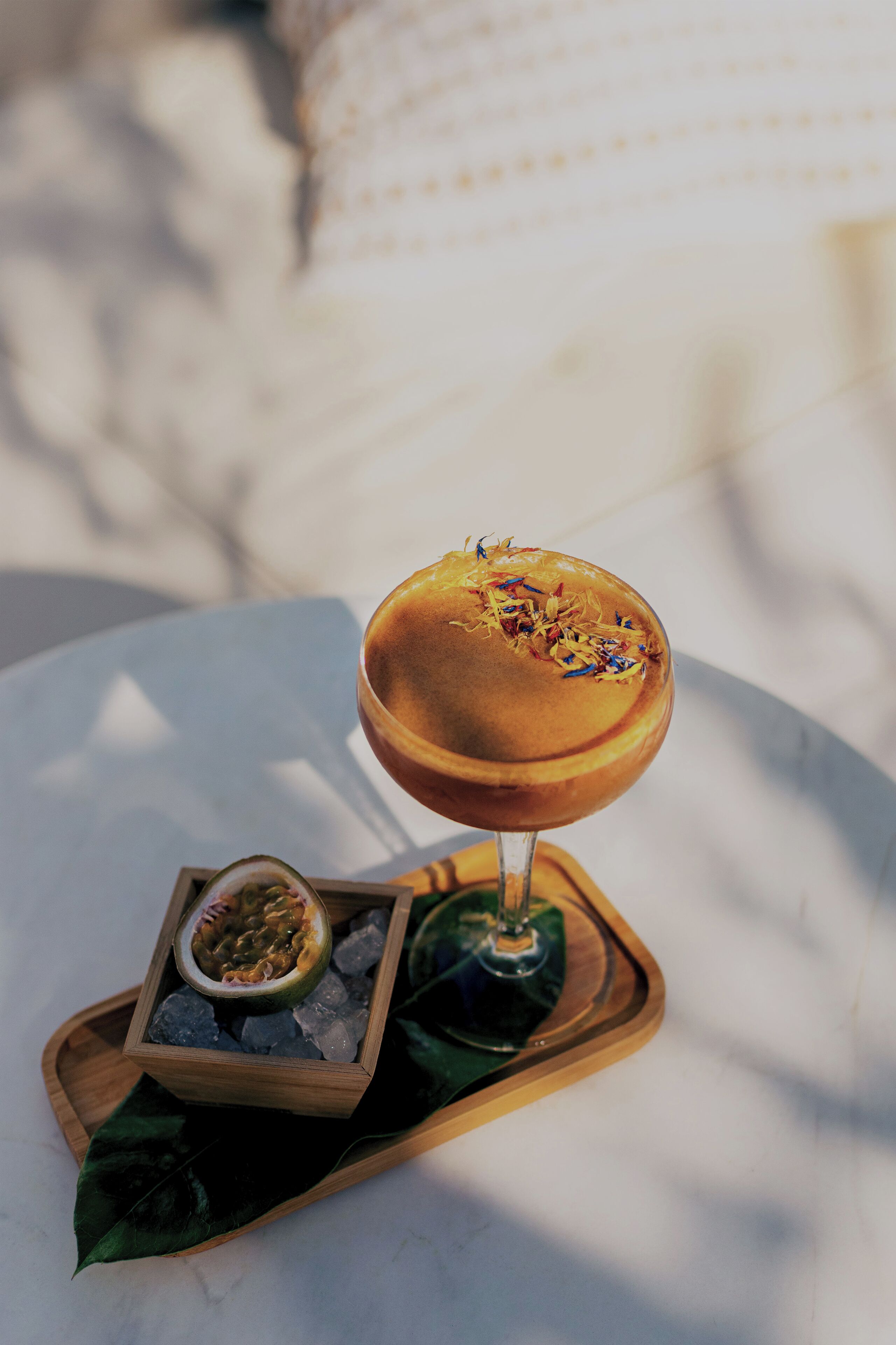 A dessert on a wooden tray with a glass of a beverage, a half-cut fruit, and some ice cubes.