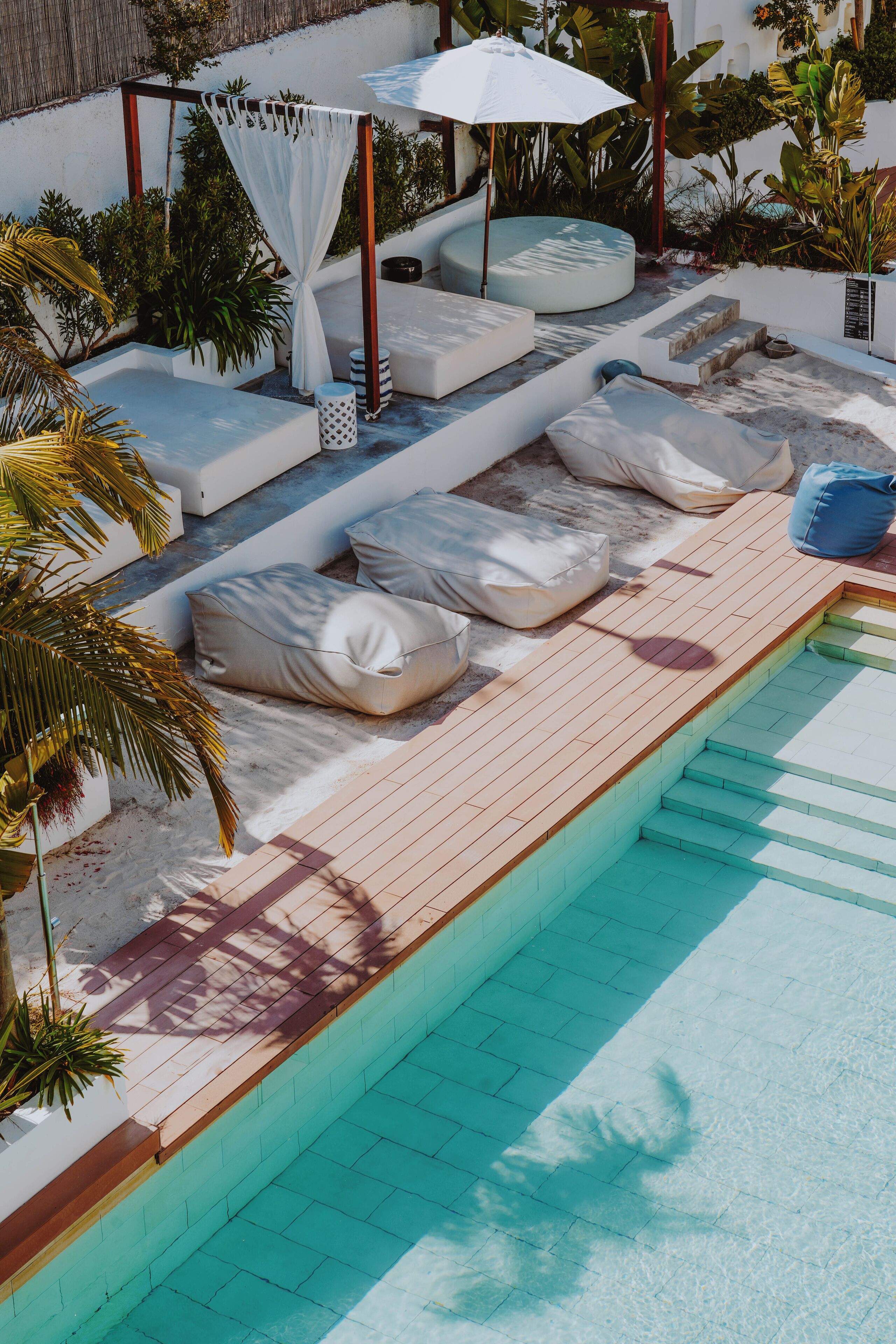 Un espace aménagé au bord de la piscine, avec des chaises longues, un auvent blanc et une terrasse en bois.
