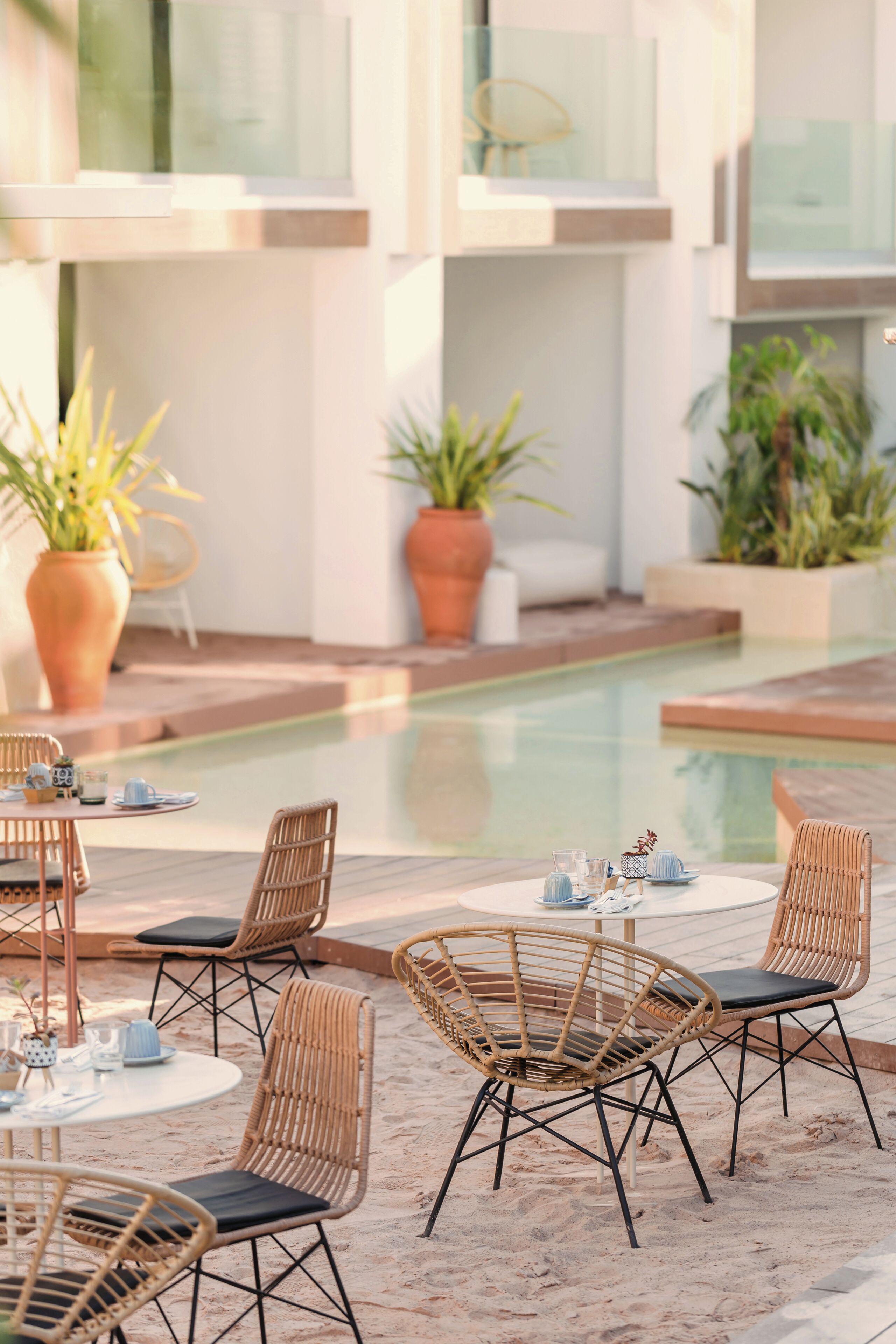 A poolside area with wicker chairs and tables, potted plants, and a clear view of the pool.