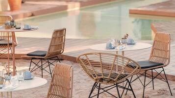 A poolside area with wicker chairs and tables, potted plants, and a clear view of the pool.