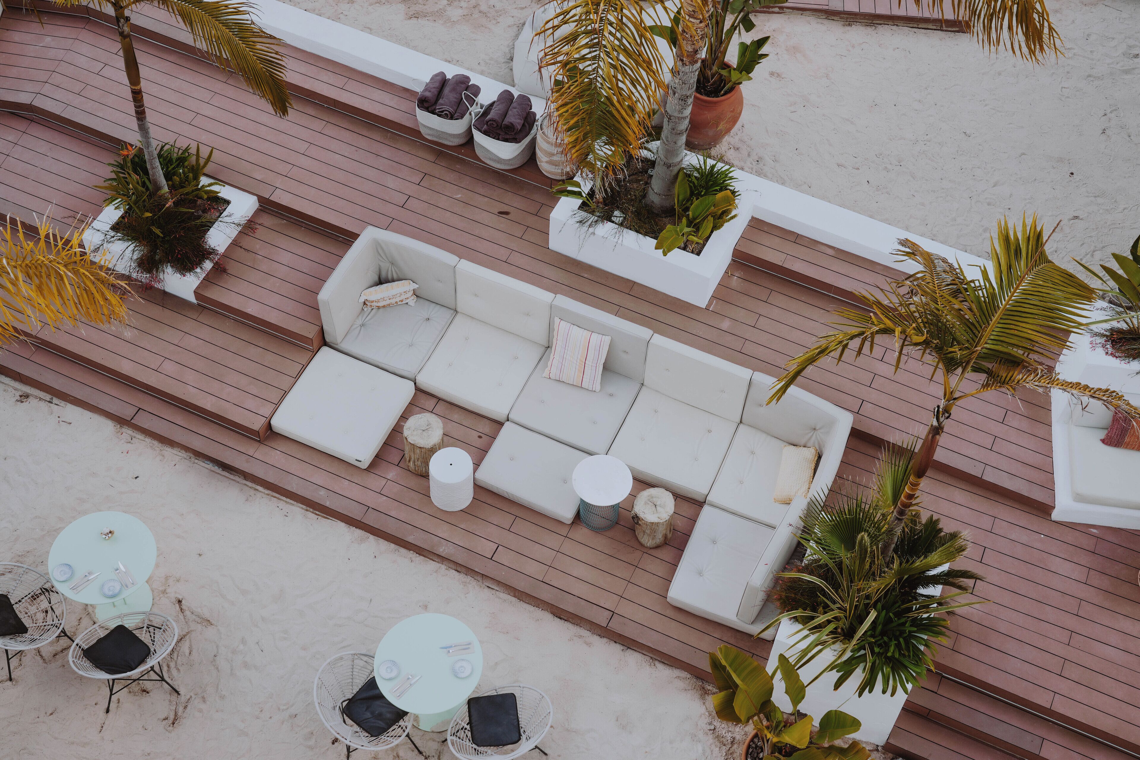 An outdoor seating area with a sofa, round tables, and chairs, surrounded by potted plants.