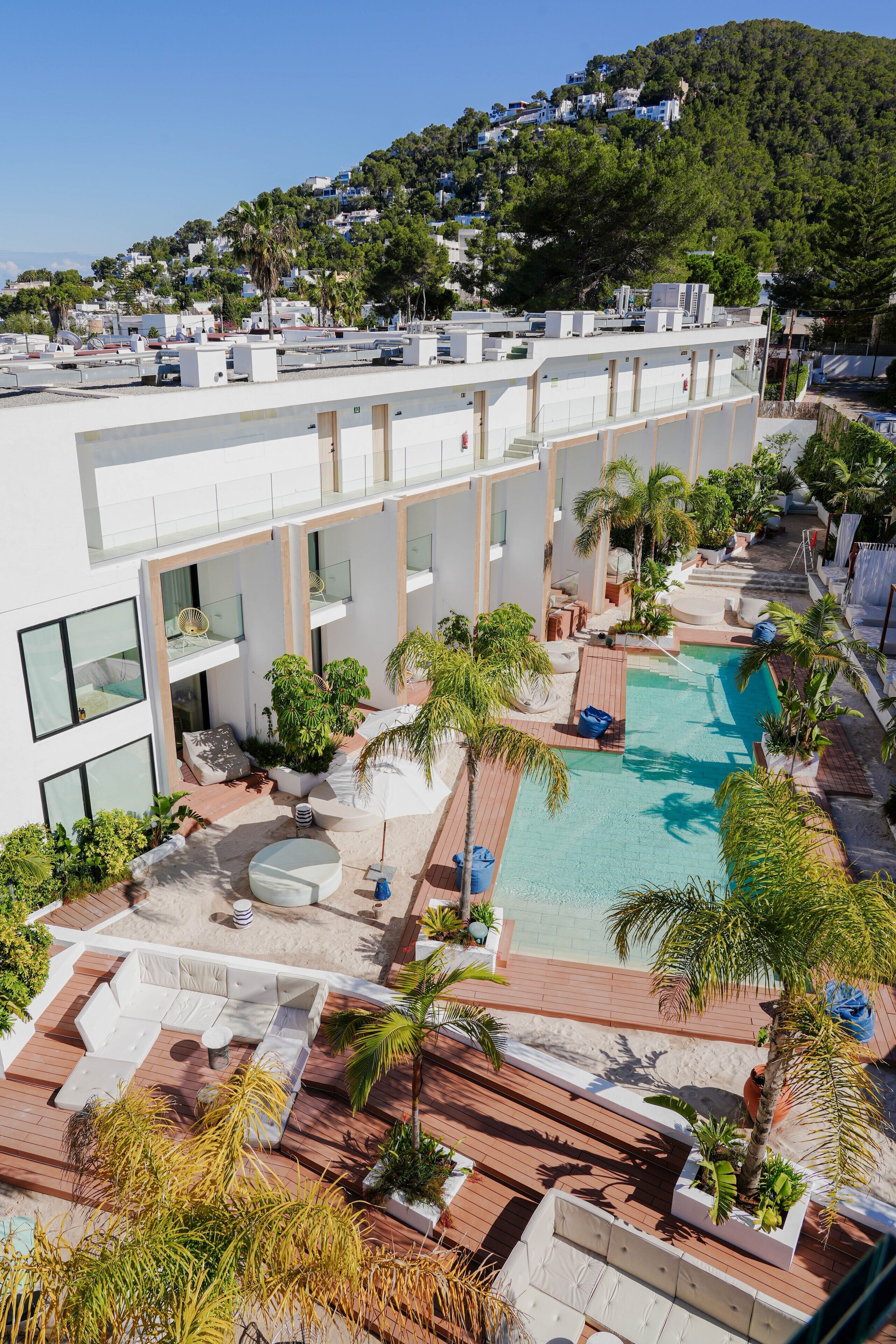 Un hotel moderno con piscina en la azotea, mobiliario exterior y abundante vegetación.