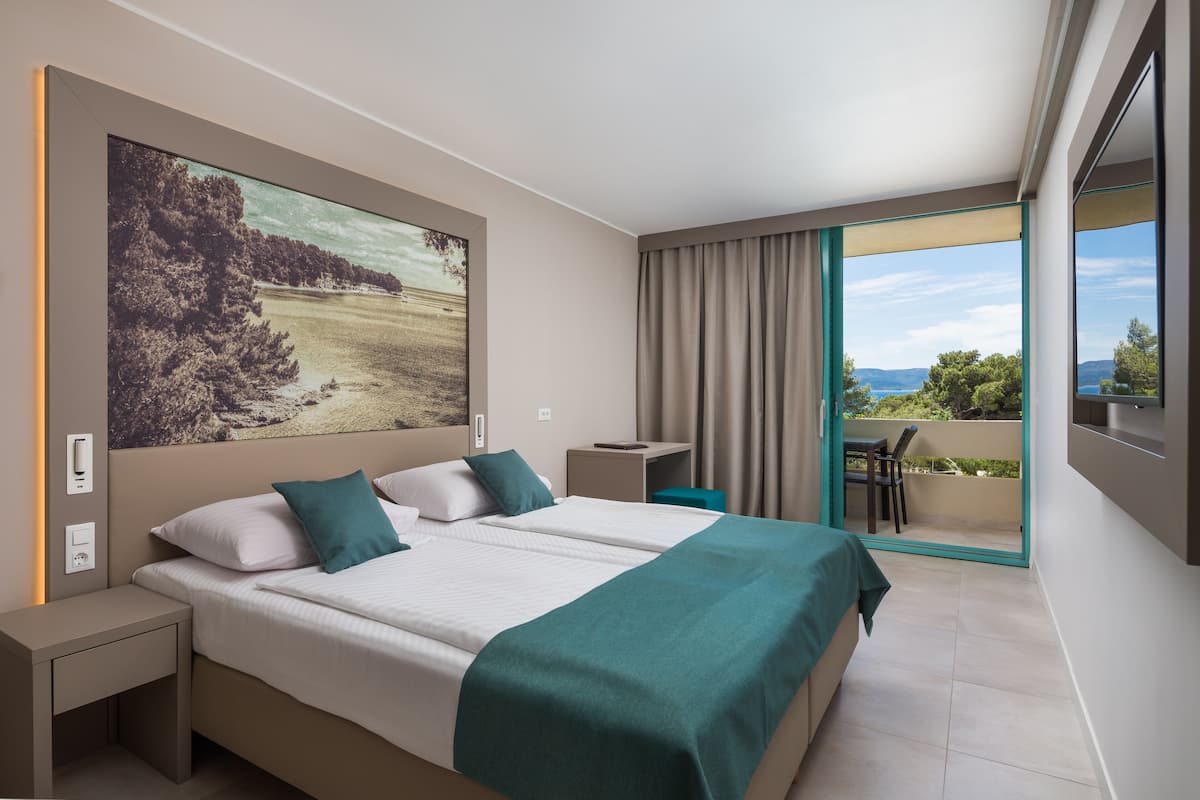 A hotel room with a large bed, a desk, a chair, and a balcony with a view.