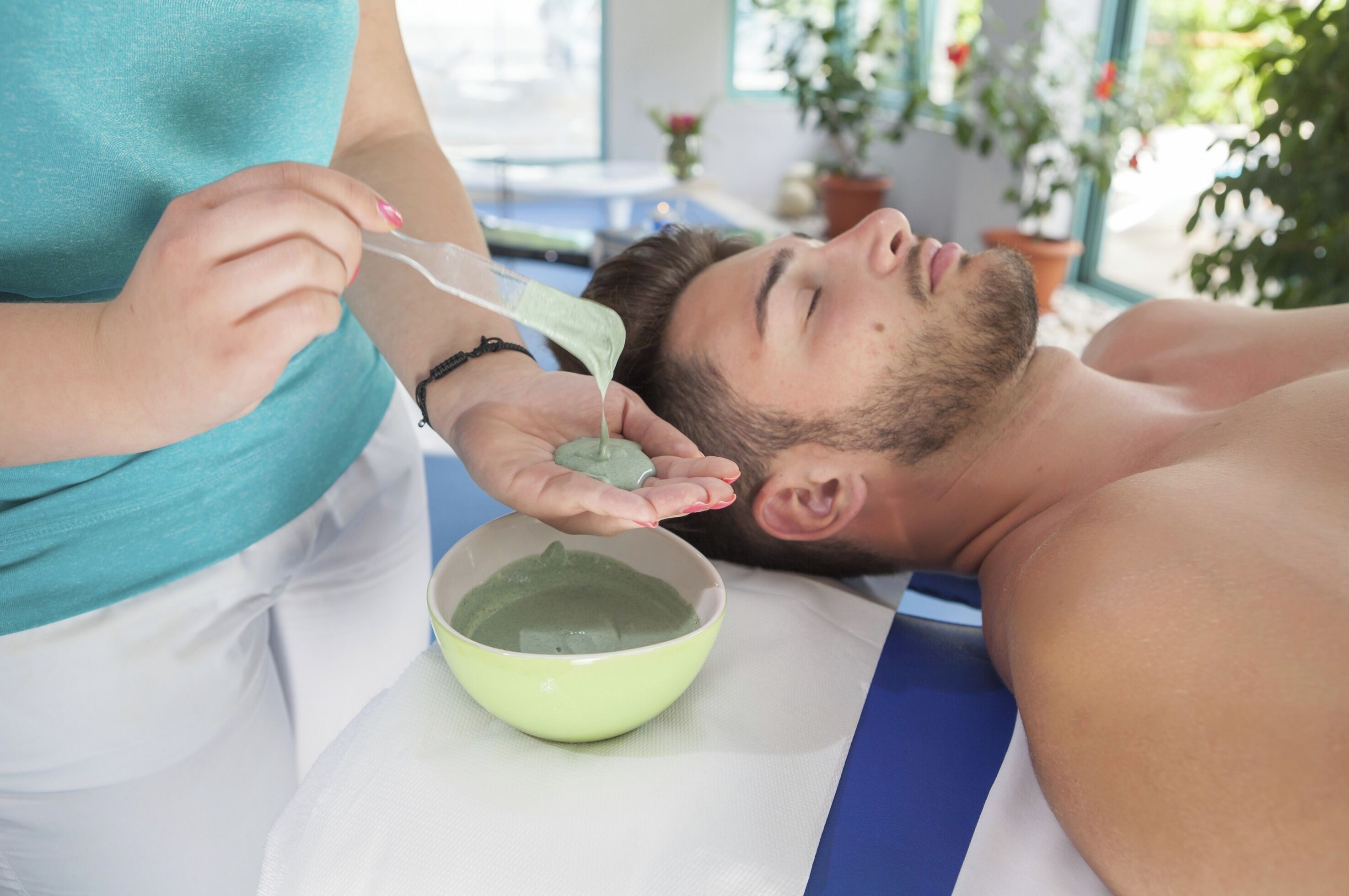 A person receiving a facial treatment with a green substance in a bowl.