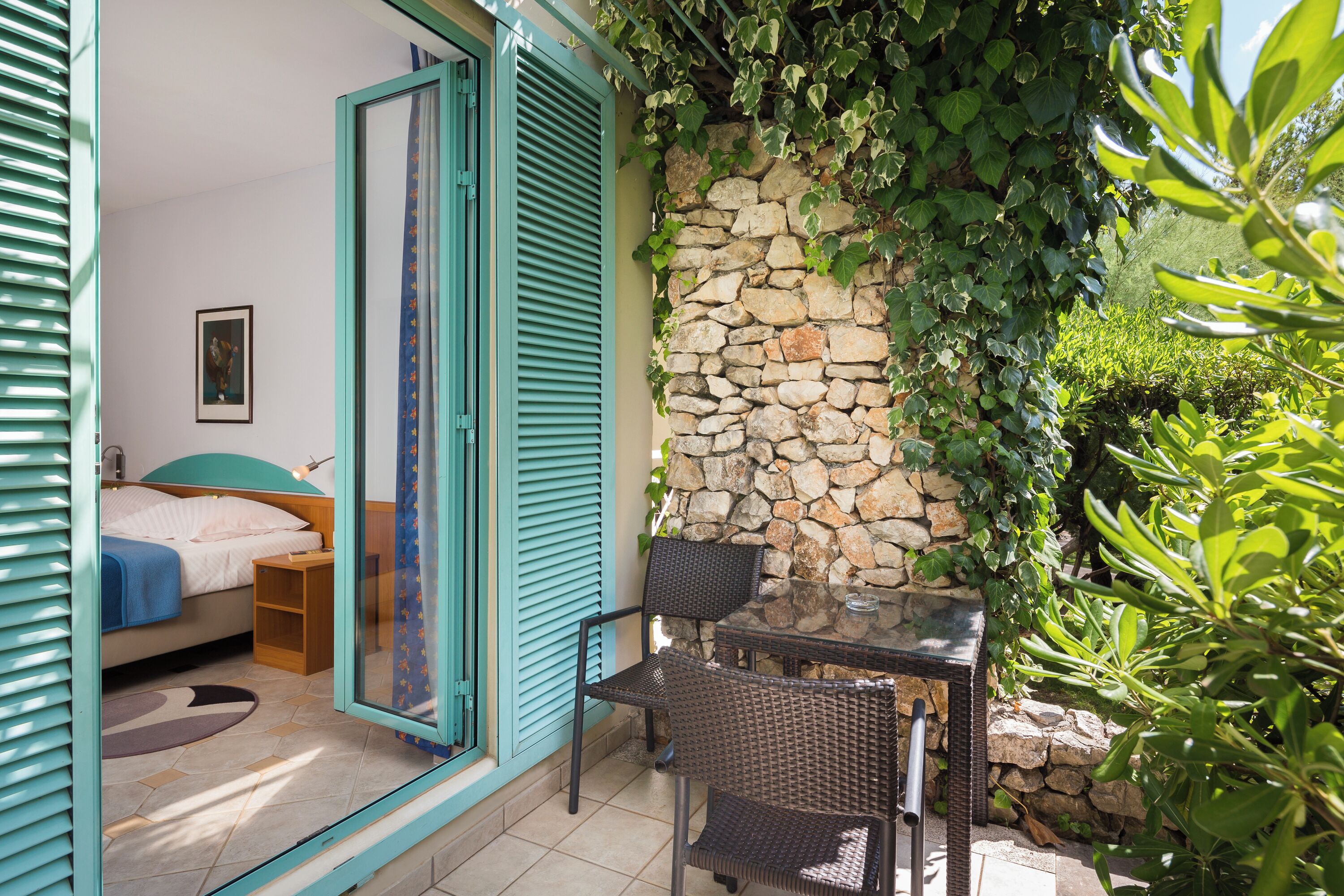 Un dormitorio con cama, mesita de noche y ventana con contraventanas azules.