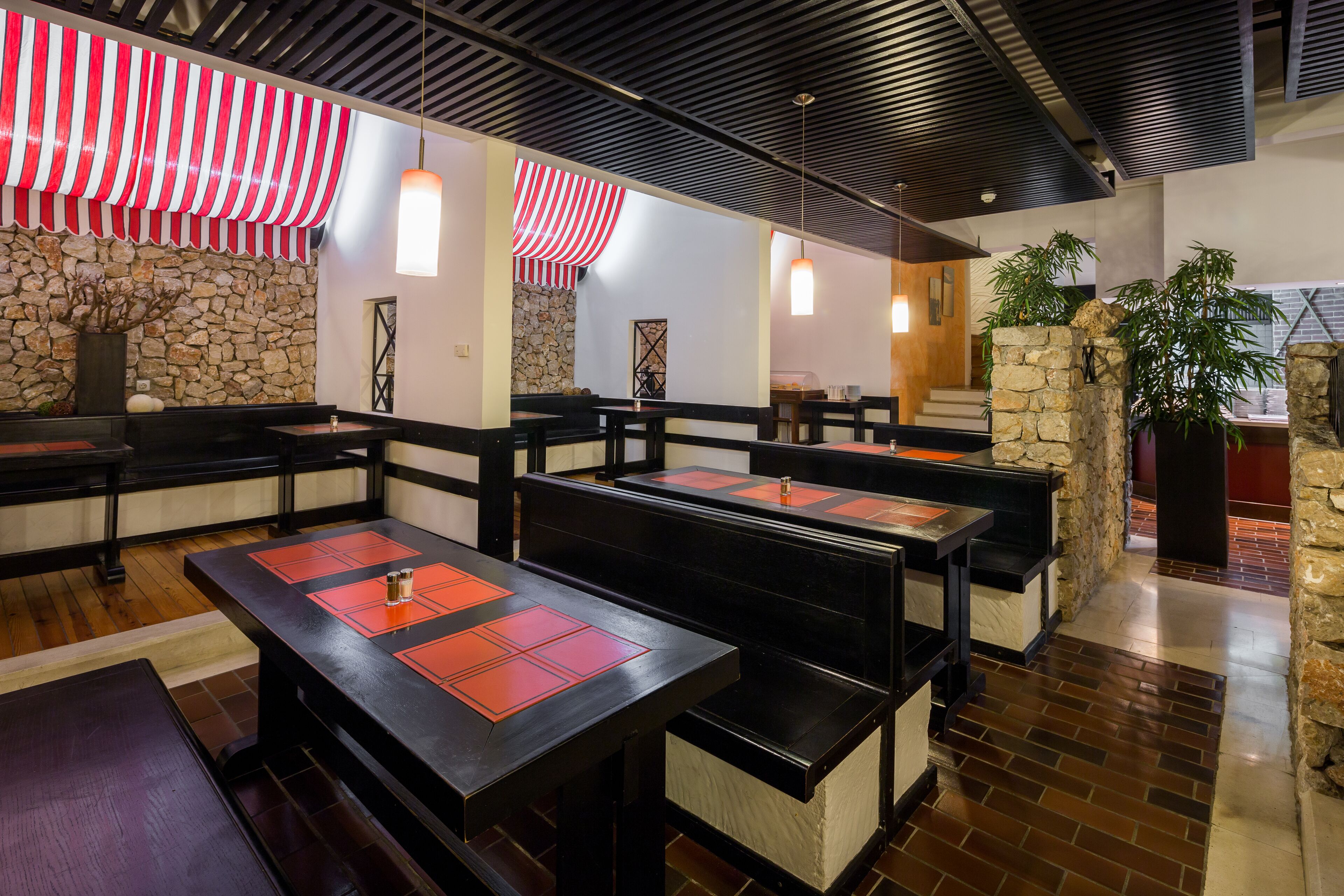 Ein Restaurant mit Holztischen und -bänken, Steinwänden und beidseitig rot-weiß gestreifter Stoffbahnen.