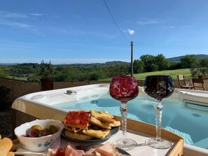 Una vasca idromassaggio con vista panoramica, un vassoio con cibo e bevande, e una ciotola di olive.