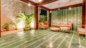 A spacious living area with a green-tiled floor, wooden furniture, and a stone wall. - Tulum Jungle Condo with Private Terrace & Jacuzzi (Tulum)