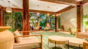 A spacious indoor area with wooden furniture, a stone wall, and a mural of a tropical garden. - Tulum Jungle Condo with Private Terrace & Jacuzzi (Tulum)