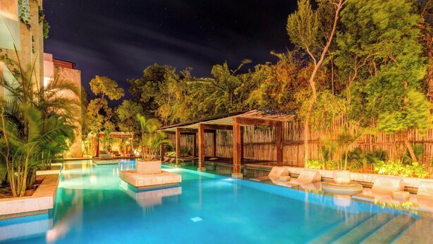 A nighttime pool area with clear blue water, surrounded by lush greenery and a wooden pergola. - Tulum Jungle Condo with Private Terrace & Jacuzzi (Tulum)