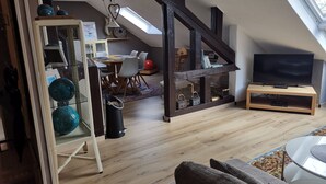 Un soggiorno in stile loft con pavimento in legno, una TV su un supporto in legno, un'area pranzo con tavolo e sedie e una scala con travi a vista.