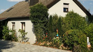 Una casa con tetto in tegole, un camino e un giardino ricco di piante e fiori.