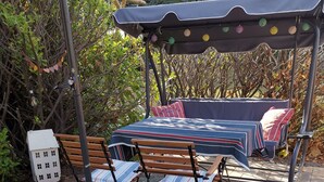 Un'area esterna con posti a sedere, un tavolo, sedie, una panchina coperta e un modellino decorativo di una casa.