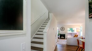 A staircase leading to a living area with a fireplace, a dining table, and a clock on the wall.