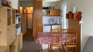 A compact kitchen with wooden cabinets, a dining table with chairs, a microwave, a kettle, and a hanging light fixture. - Cozy Studio with Balcony, Near Slopes and Shops, Ski-in/Ski-out Access (Le Pleynet)