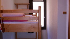 A bunk bed room with a wooden headboard, a small table, and a window. - Cozy Studio with Balcony, Near Slopes and Shops, Ski-in/Ski-out Access (Le Pleynet)