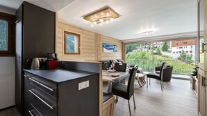 Een moderne keuken met een inbouwfornuis, een eethoek met tafel en stoelen, en een balkon met uitzicht op de omgeving.