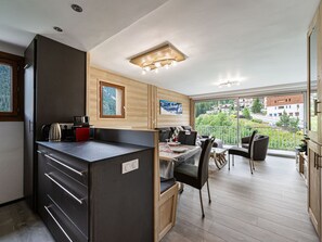 Een moderne keuken met een inbouwfornuis, een eethoek met tafel en stoelen, en een balkon met uitzicht op de omgeving.