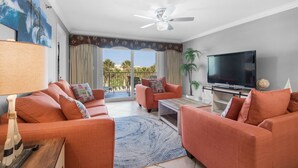 Ein Wohnzimmer mit orangefarbenen Sofas, einem Flachbildfernseher, einem Deckenventilator und Blick ins Freie.