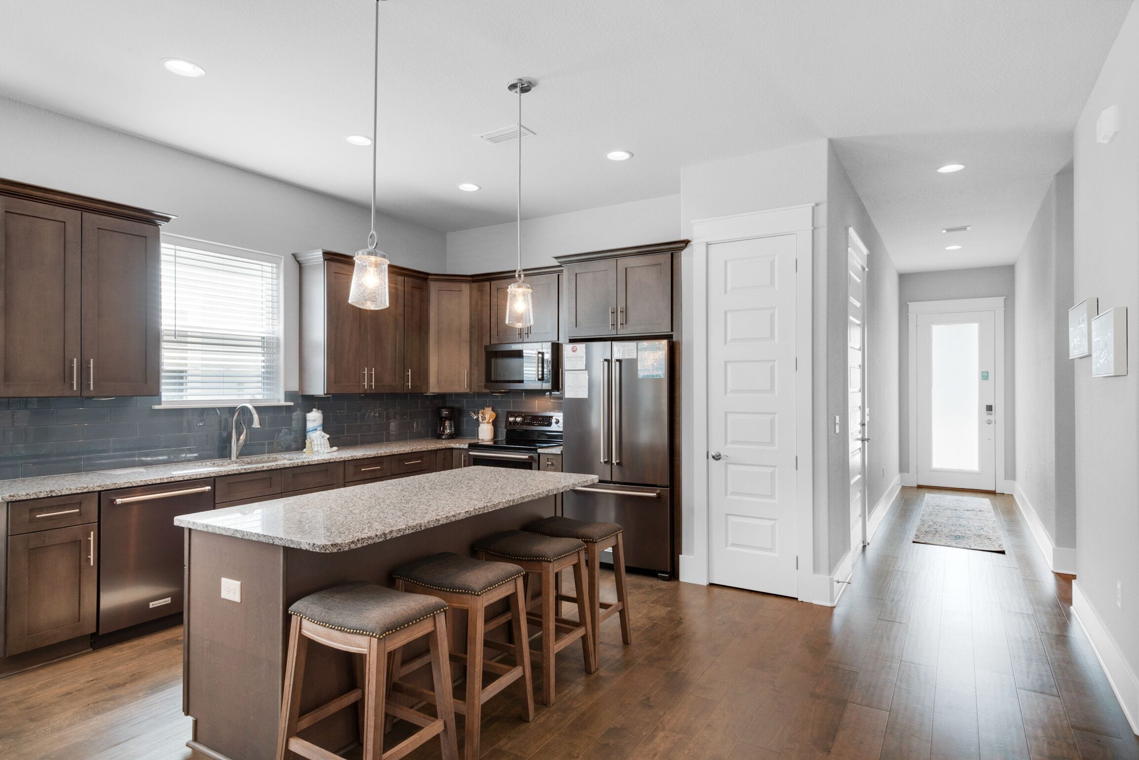A modern kitchen with dark wooden cabinets, a granite countertop, and stainless steel appliances. There are three bar stools at the island.