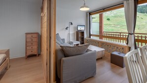 A cozy room with a bed, a sofa, a TV, and a window with a view of a green landscape.