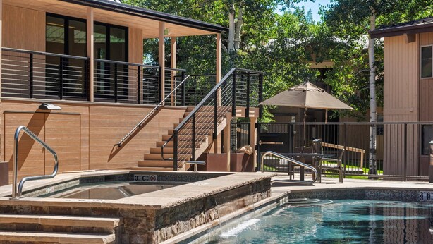 A swimming pool with steps leading into it, a covered seating area, and a building with a wooden facade and a staircase. - Access to Snowmass Mtn Via Trail! Balcony W/ Stunning Views, Pool/Hot Tub, Loft, Wood FP & Parking (Snowmass Village)