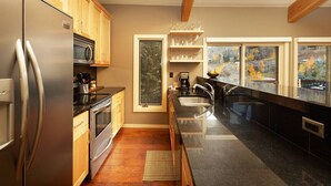 A modern kitchen with wooden cabinets, stainless steel appliances, a large window with a view, and a black countertop. - Access to Snowmass Mtn Via Trail! Balcony W/ Stunning Views, Pool/Hot Tub, Loft, Wood FP & Parking (Snowmass Village)