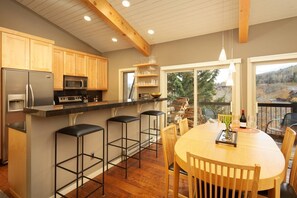 A modern kitchen with wooden cabinets, stainless steel appliances, and a bar area with stools. - Access to Snowmass Mtn Via Trail! Balcony W/ Stunning Views, Pool/Hot Tub, Loft, Wood FP & Parking (Snowmass Village)