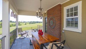 A covered patio with a wooden table and chairs, a brick wall, and a view of a green landscape. - Dog-Friendly Shelby Park Home · 3BR Sleeps 8 (Nashville)