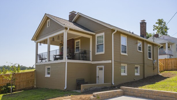 A two-story residential building with a covered porch, a brick chimney, and a fenced yard. - Dog-Friendly Shelby Park Home · 3BR Sleeps 8 (Nashville)