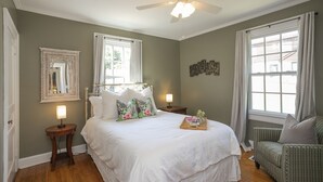A bedroom with a bed, a nightstand, a chair, a ceiling fan, and a window with curtains. - Dog-Friendly Shelby Park Home · 3BR Sleeps 8 (Nashville)