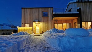 Un edificio moderno con fachada de madera, entrada visible y suelo cubierto de nieve.