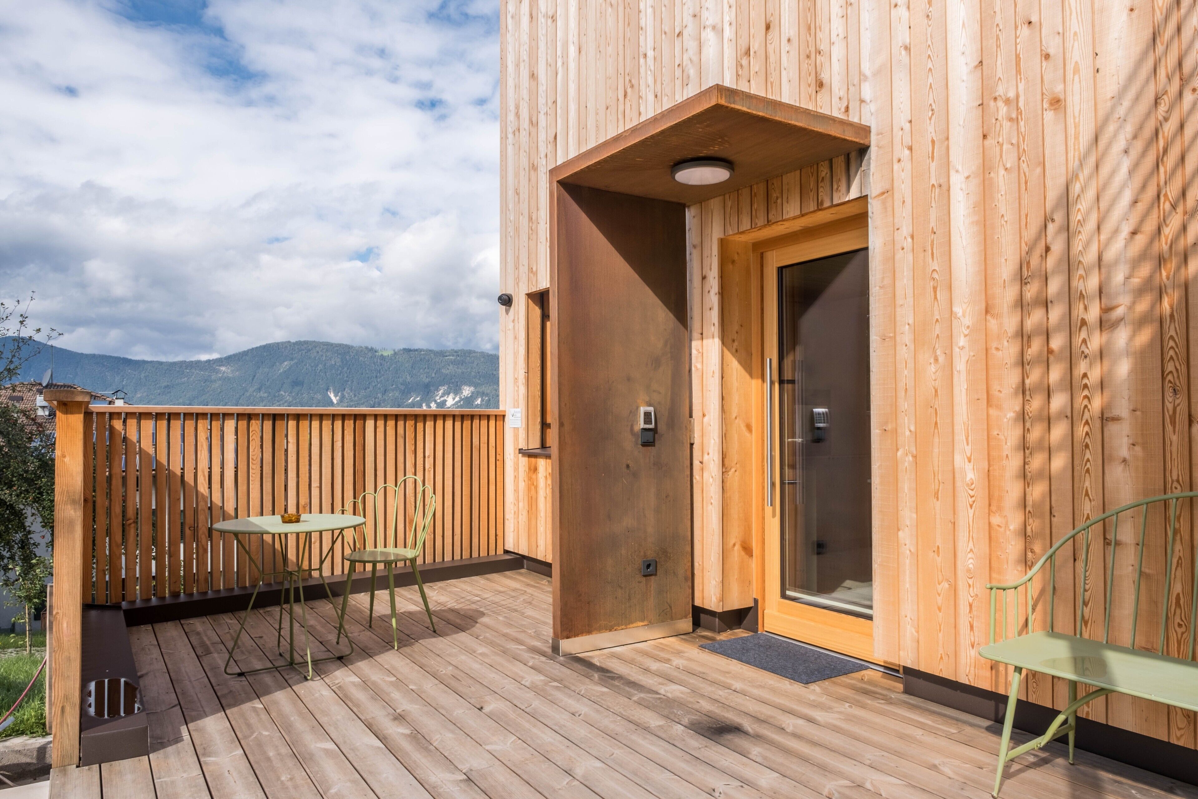 Une terrasse en bois avec une table et des chaises, une porte et une vue sur les montagnes.