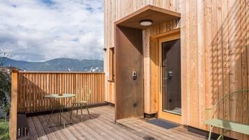 Une terrasse en bois avec une table et des chaises, une porte et une vue sur les montagnes.