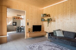 Un salon moderne avec un mur en bois, un téléviseur à écran plat, un canapé et un coin repas comprenant des chaises et une table.