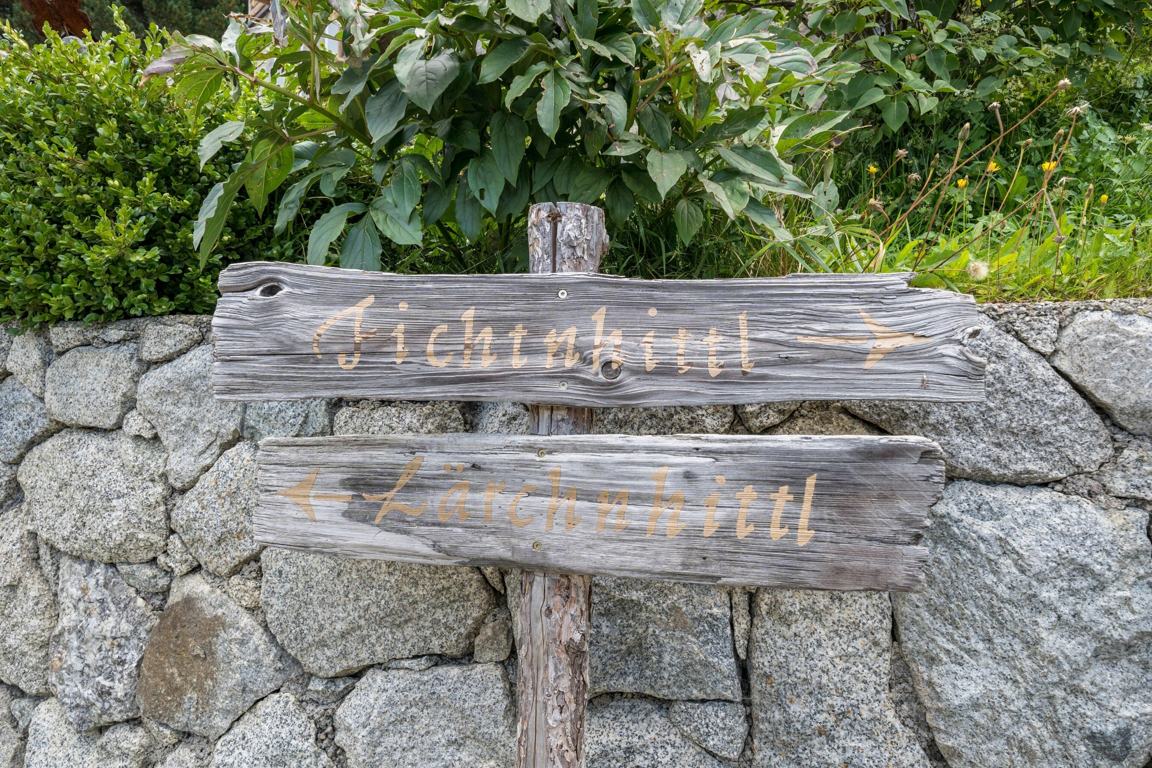 Un panneau indicateur en bois, muni de flèches directionnelles et d’inscriptions indiquant « Fichtnittl » et « Lärchnhitl ».
