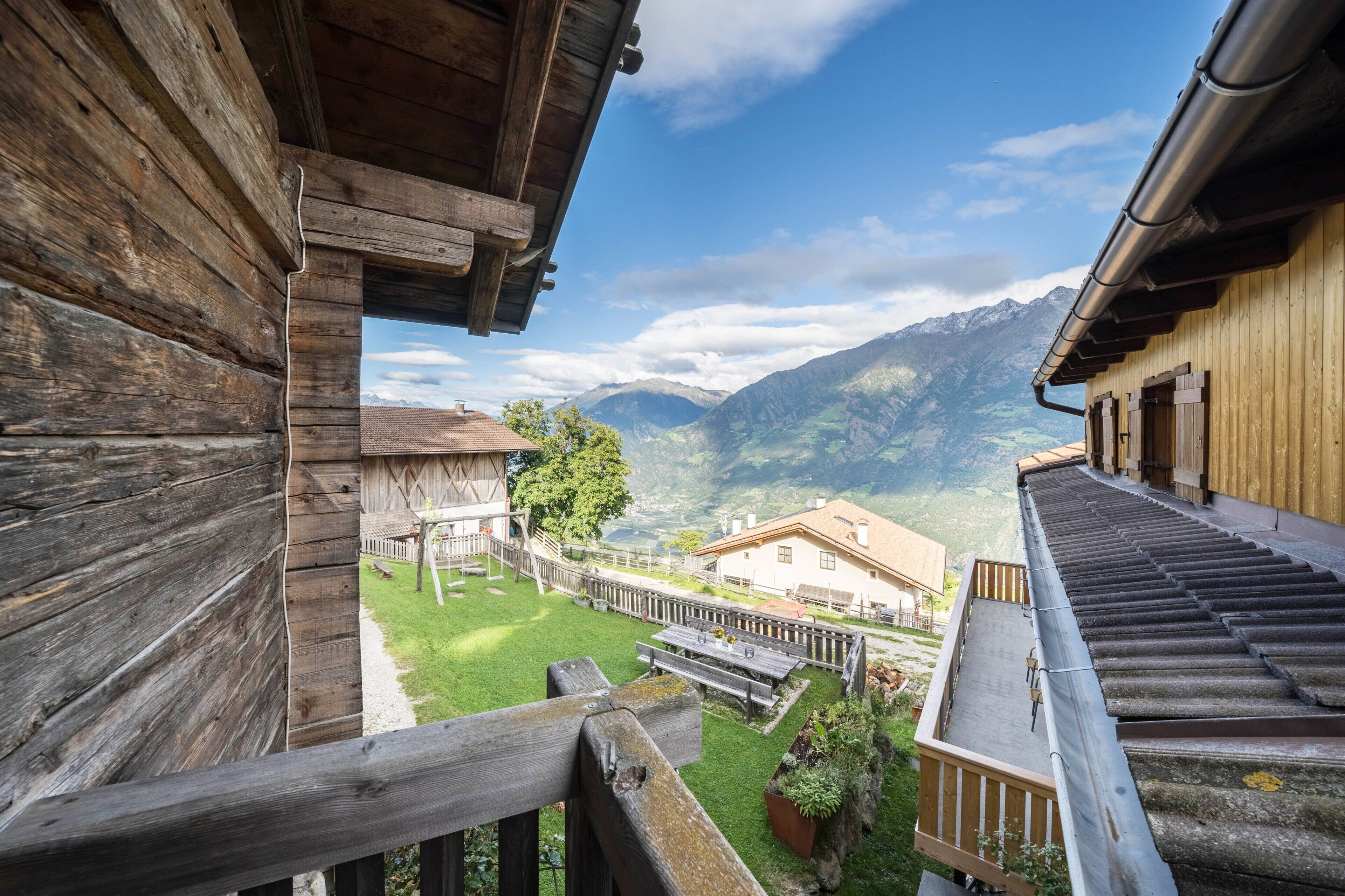A wooden building with a view of mountains and a grassy area with benches.